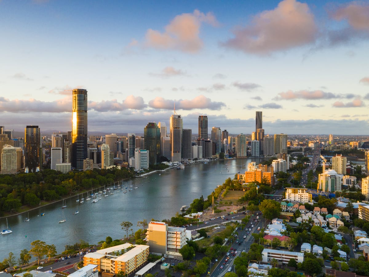 Vista aérea panorámica del río Brisbane serpenteando a través de la ciudad de Brisbane, Australia, rodeado de rascacielos modernos, parques verdes y zonas residenciales durante el atardecer.