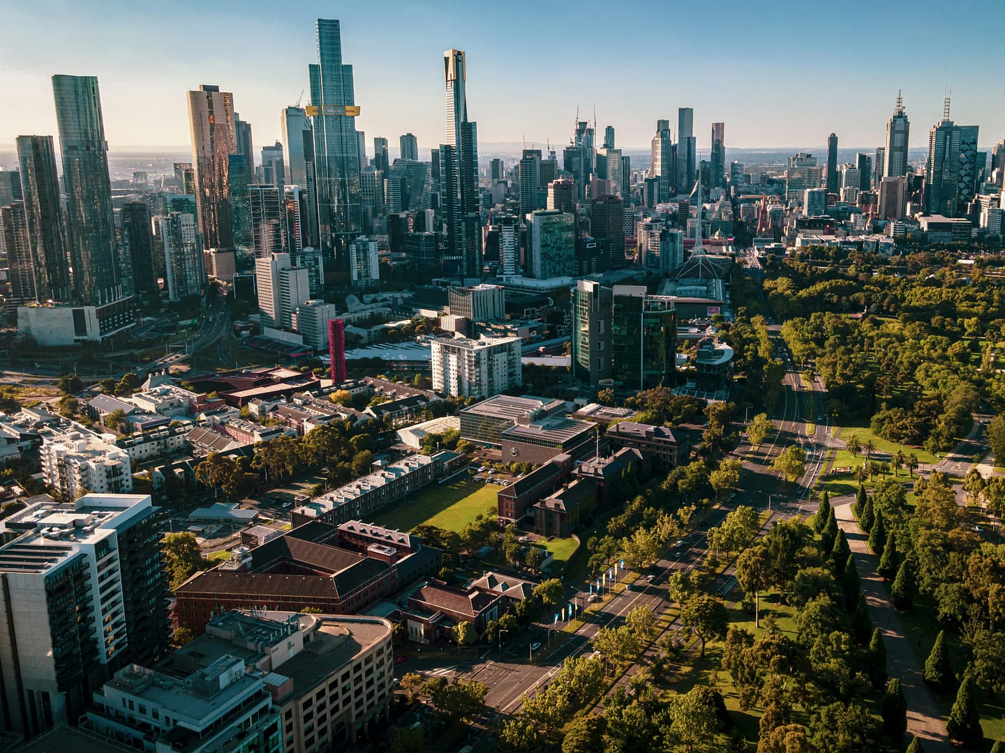 Línea de rascacielos de la ciudad de Melbourne, Australia, rodeada de parques arbolados y áreas verdes.