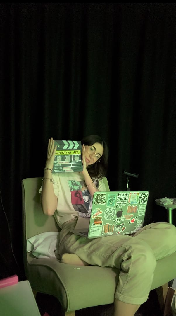 Estudiante de cine sosteniendo una claqueta de cine, con una cortina oscura de fondo.