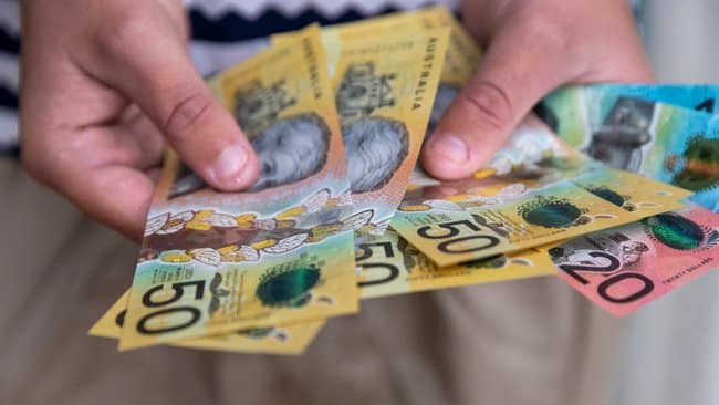Manos sosteniendo varios billetes de dólar australiano de diferentes denominaciones y colores.