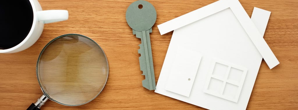 House and key shaped paper cutout, calculator and magnifier on wooden table.