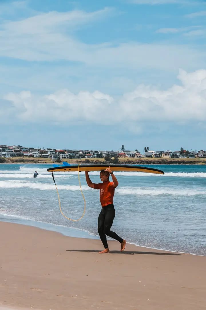 Estudiante con tabla de surf en una playa Australiana 
