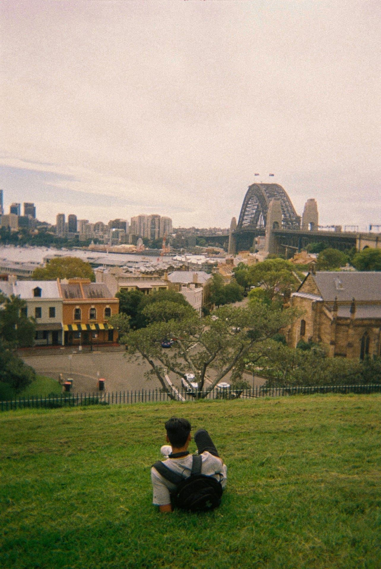 estudiante acostado en una colina con vista al Sydney Harbour Bridge